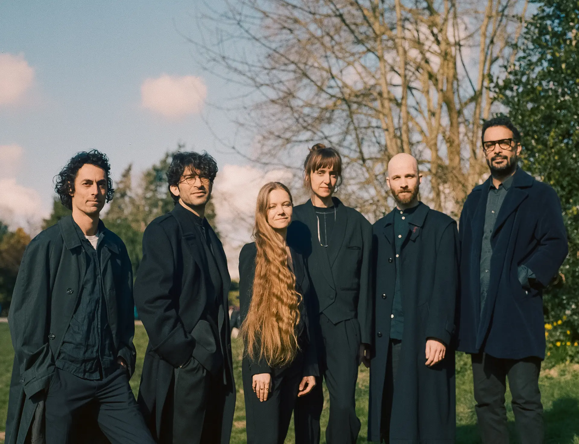 Group photo of the artists from 'About That Magic Circle,' including Yunah Proost, standing together in nature, all dressed in black.